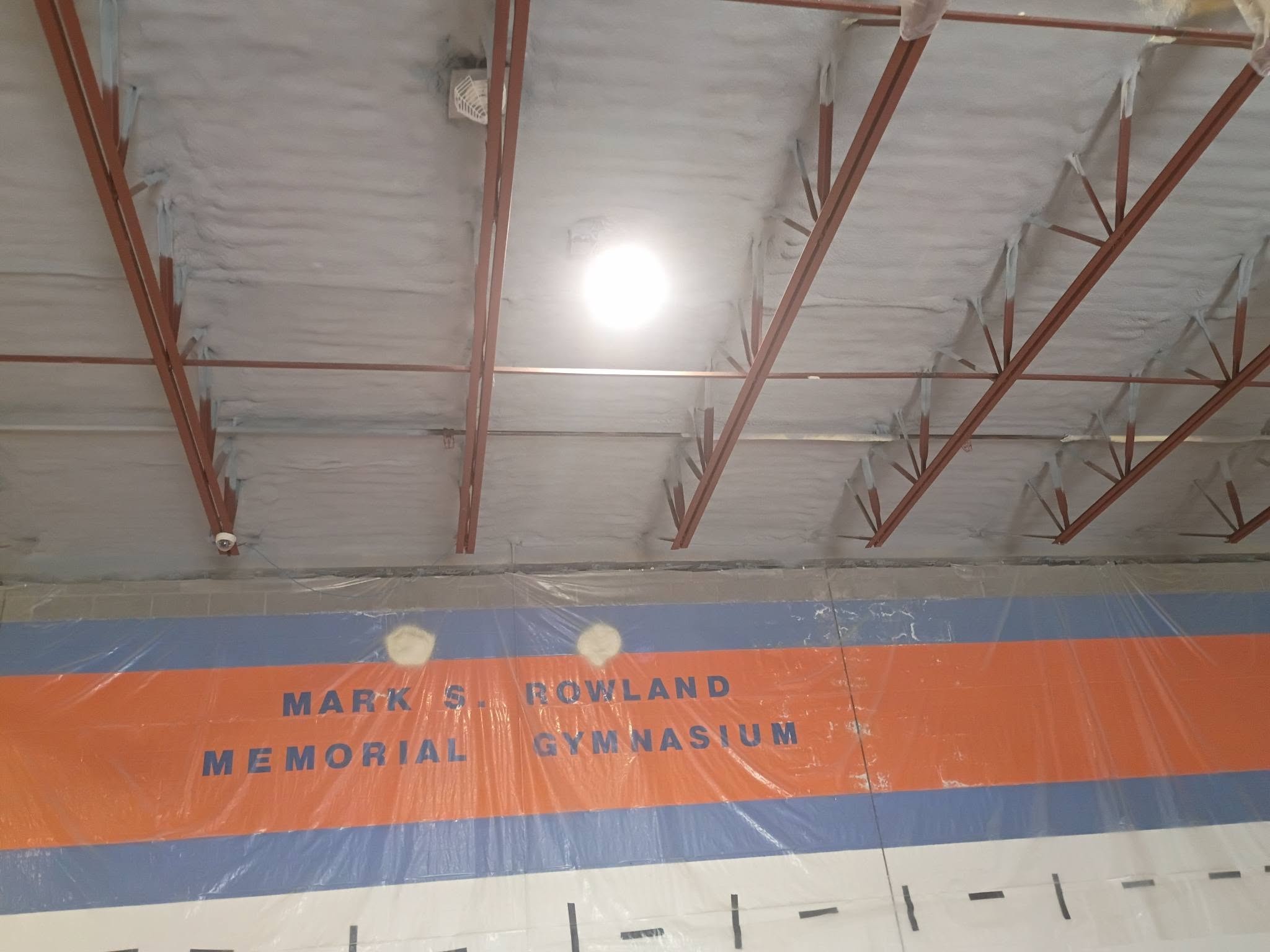 Protected gymnasium walls and lighting below spray foam insulation work in Nashua New Hampshire